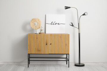 Wooden cabinet with decor and standard lamp near white wall