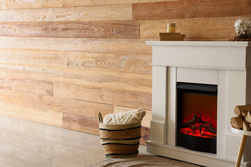 Stylish fireplace and basket with soft pillow near wooden wall