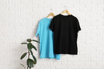 Stylish t-shirts hanging on white brick wall