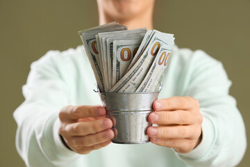 Young man with bucket of dollar banknotes on green background, closeup © Pixel-Shot