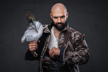 A bald pirate with a black beard wearing a vest, holding a hat against a textured dark wall