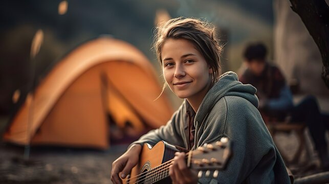 Young woman tourist plays guitar music and sings song near a tent in a camping. Travel adventure tourism and freedom concept. - Powered by Adobe