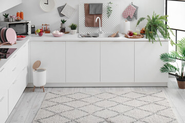 Interior of modern kitchen with stylish rug, trash bin and white counters