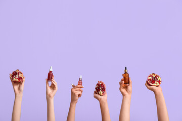 Female hands holding cosmetic products and pomegranate on lilac background