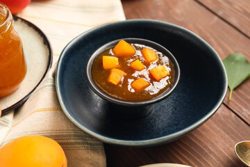 Bowl with sweet apricot jam on wooden background