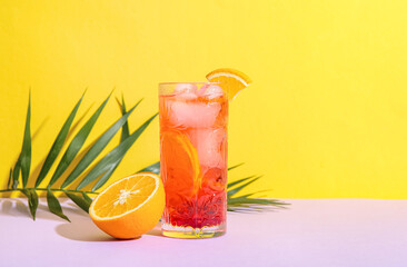 Glass of tasty Negroni cocktail, orange and palm leaf on color background