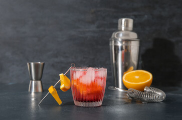 Glass of cold Negroni cocktail and bartender tools on dark background