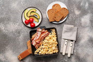 Frying pan of tasty scrambled eggs with bacon on grey background