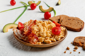 Plate of tasty scrambled eggs with bacon on white background
