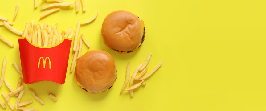 Kyiv, Ukraine - August 10, 2023: French fries in paper packaging and burgers on a yellow background, top view. McDonald's Corporation is the world's largest fast food restaurant. Copy space