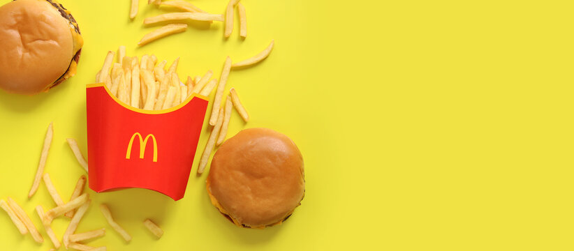 Kyiv, Ukraine - August 10, 2023: French fries in paper packaging and burgers on a yellow background, top view. McDonald's Corporation is the world's largest fast food restaurant. Copy space