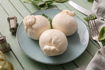 Plate of tasty Burrata cheese with basil on green wooden table