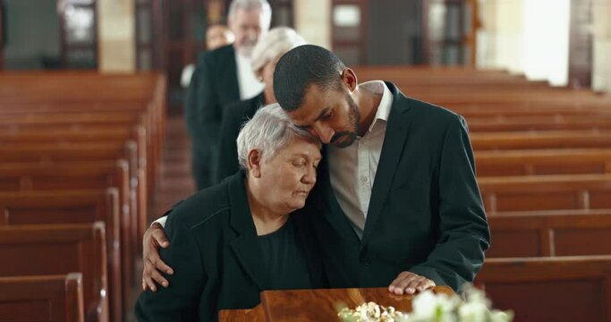 Church, funeral and senior mother and man hug for mourning death by coffin. Grief, family and son with mom by casket to console, support or interracial empathy for depressed or sad elderly woman
