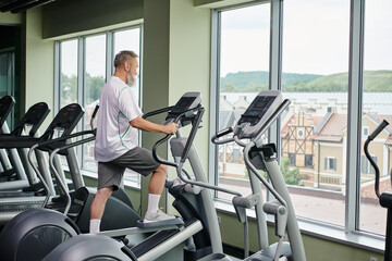 bearded man working out on stepper machine, elderly in gym, active senior, fitness and sport