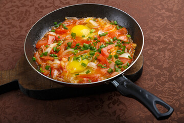 hot shakshuka in a frying pan sprinkled with green onions on a wooden board.