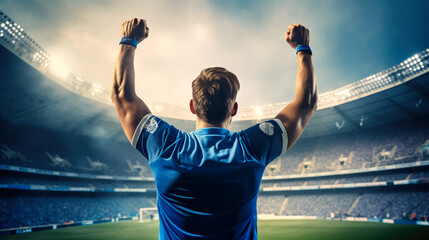 Fototapeta na wymiar Football player in a blue t-shirt celebrating a victory with raised hands in the stadium 