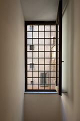 A narrow hallway in a building with a black metal grid window with light streaming in