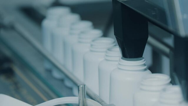 4K conveyor with moving empty white plastic tubes on the production line and filling with capsules. Automatic machine in the factory. Modern High-Tech Pharmacology Factory. Close Up, DOF