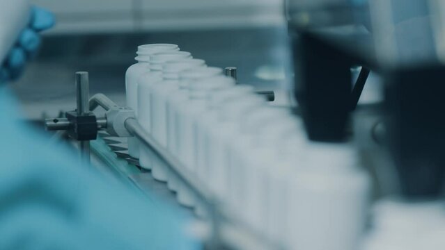 4K conveyor with moving empty white plastic tubes on the production line and filling with capsules. Automatic machine in the factory. Modern High-Tech Pharmacology Factory. Close Up, DOF