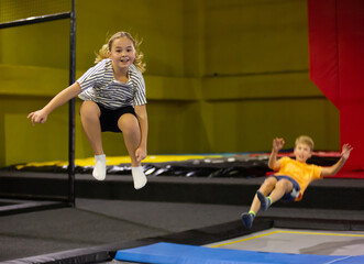 Happy emotional tween girl having fun in indoor amusement park, bouncing on trampoline..