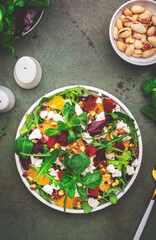 Beet and feta cheese salad with arugula, lettuce, orange and pistachios on green table. Fresh useful dish for healthy eating