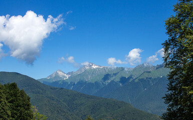 Naklejka premium beautiful panoramic mountain landscape with rock tops among green trees on a sunny summer day with white clouds and copy space in krasnaya polyana sochi russia