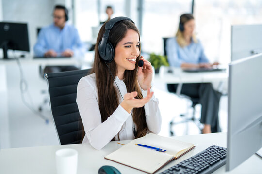 IT service desk female operator talking to client using headset and working on computer in call center office.
