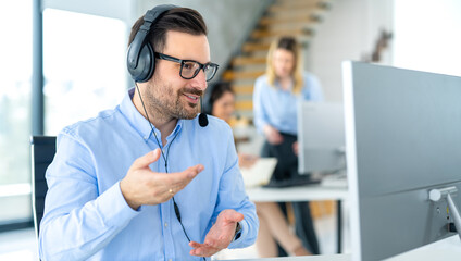 Focused middle aged handsome man in formal shirt and headset working on computer in call center...
