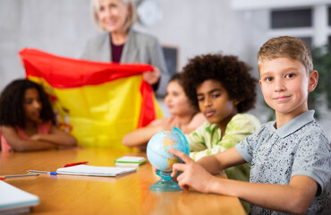 Fototapeta premium Portrait of a schoolboy in class, studying the history of the country of Spain in lesson and looking for it on the globe