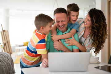 Ecstatic young family laughing and playing with their children in front of laptop while hugging...