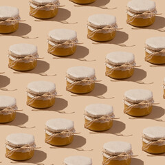 Pattern from glass jar with honey under kraft paper on a string on beige background. Sweet food monochrome concept.