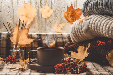 Atmospheric cozy autumn composition. Hot mug of coffee, book, fall leaves, chestnut, ashberry, acorns and cozy brown plaid as background. Sunday loneliness relaxing, hugge mood. Thanksgiving day.