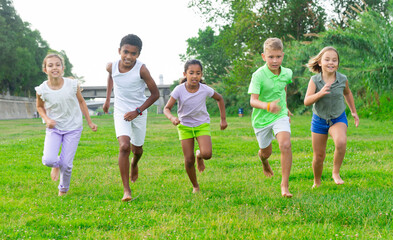 Fototapeta premium Positive kids playing active games in summer park chasing each other