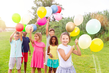 Fototapeta na wymiar Portrait of happy preteen girl holding colorful helium balloons in hands, having fun with friends on green lawn on summer day
