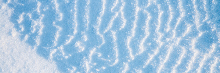 Beautiful winter background with snowy ground. Natural snow texture. Wind sculpted patterns on snow surface. Wide panoramic texture for background and design.