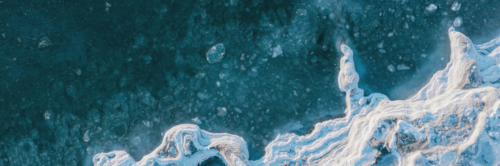 Top view of the freezing sea. Winter aerial photograph of an icy shore and ice in sea water. Northern nature. Cold frosty winter weather. Harsh arctic climate. Beautiful wide panoramic background.