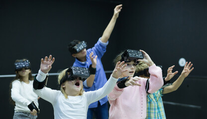 Modern cheerful tweenagers wearing virtual reality goggles playing video games together
