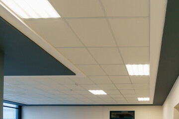 White suspended ceiling and square fluorescent lamps in the office. Interior design of a spacious...
