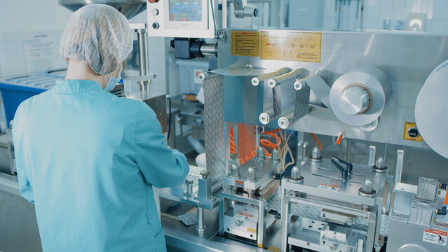4K Blister Packing Machine. Woman works at the workplace. Tablet pharmaceutical blister packaging machine in supplement drug manufacture. Pharmaceuticals production line