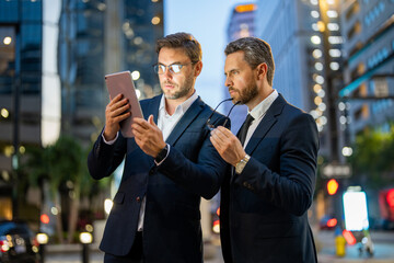 Night business in city. Business men check their emails and review important documents on tablet on night city. Business, technology and people concept. Businessman showing tablet to colleague.