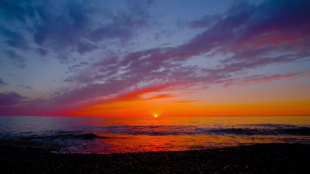 Timelapse: amazing dramatic sunset over the Black Sea surface in the evening, getting darker. Moving clouds in the sky. Waves is crashing on the pebble beach. Cloudscape, summer and time lapse concept