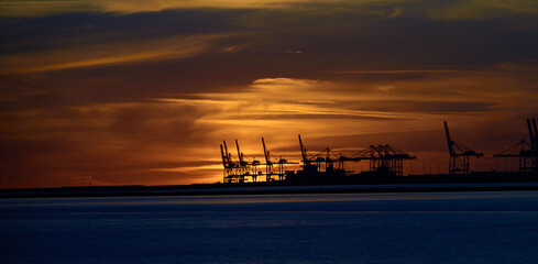 Le Havre port cranes back-lit by orange sky and clouds of a distant sunset