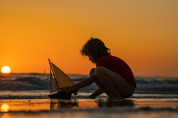 Child playing with a toy boat. Little kid boy sailing toy ship on sea water. Summer vacation with kids. Kid dreaming about sailing. Adventure and travel with children. © Volodymyr