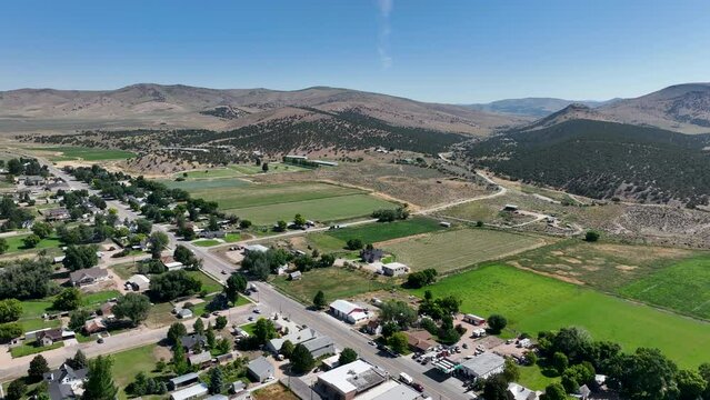 Rural town main street homes to farms Utah overhead. Farming community agricultural economy. Spring summer weather mountain valley green agriculture field. Homes, barns and buildings.