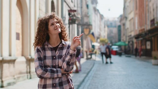 Thoughtful young woman showing pointing empty place advertising area for commercial text copy-space for goods promotion. Girl tourist pondering a solution, inspiration dreaming outdoors in city street
