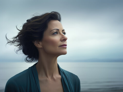 A portrait of a middleaged woman looking out onto a vast empty expanse of sea her gaze showing the emptiness she feels inside.