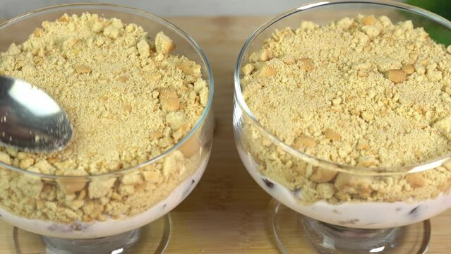 Assembling a puff dessert in a glass bowl and sprinkling with crumbled biscuits, creamy cream sweets. Cooking at home