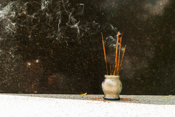 Smoking incense sticks in a glass vase. Festive incense near the marble Buddha statue. An offering...