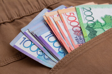 Paper multicolored money of republic of kazakhstan in pocket of brown denim jeans. Textile background. Vacation cash, salary, currency exchange, immigration, travel, trip, bribe, loan. Kazakh tenge