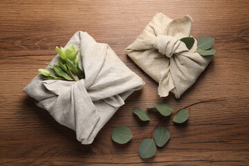 Furoshiki technique. Gift packed in different fabrics decorated with plants on wooden table, flat lay